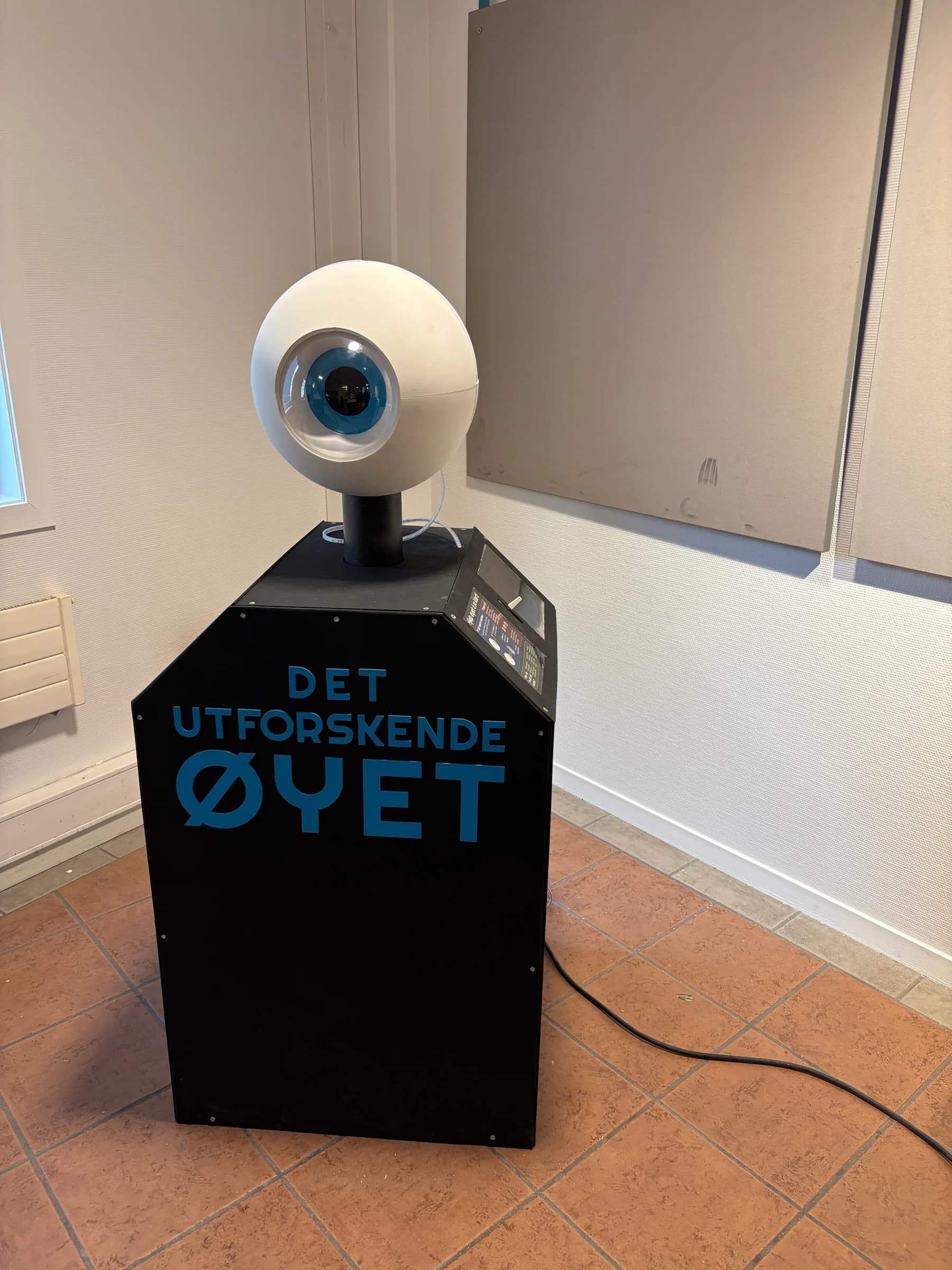 Installasjonen Det utforskende øyet: et stort øye på en svart sokkel med blå bokstaver